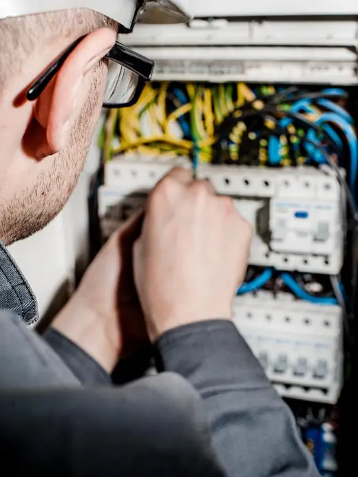 An electrician in a hard hat and safety glasses working on the breaker switches inside a switchboard.