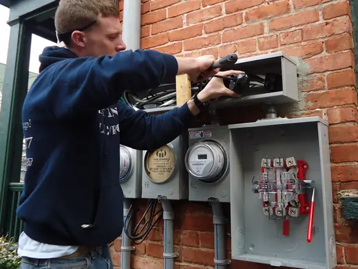 A Redgum electrician working on a meter and connection box on the side of a brick building.