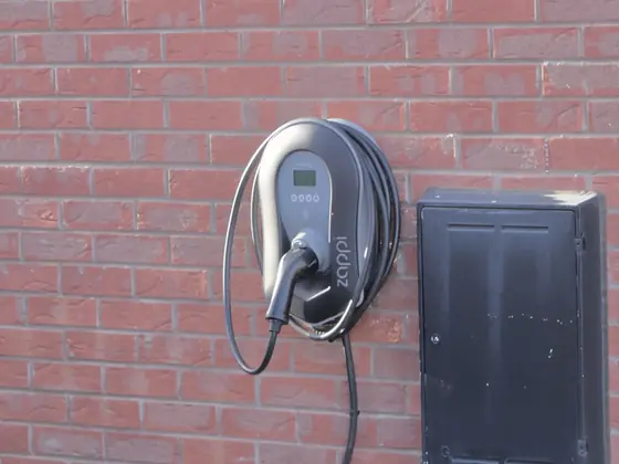 A wall-mounted home EV charger with its cable coiled neatly, fitted to a brick wall.